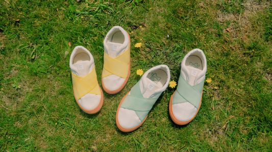 yellow and green sustainable kids shoes on green grass with spring daisy among them