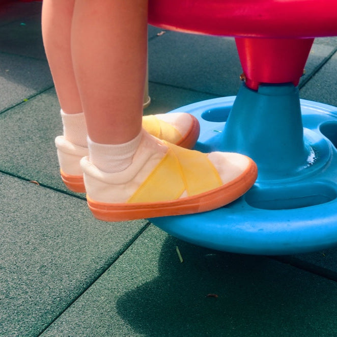 Child's feet wearing sustainable sneakers on a playground surface