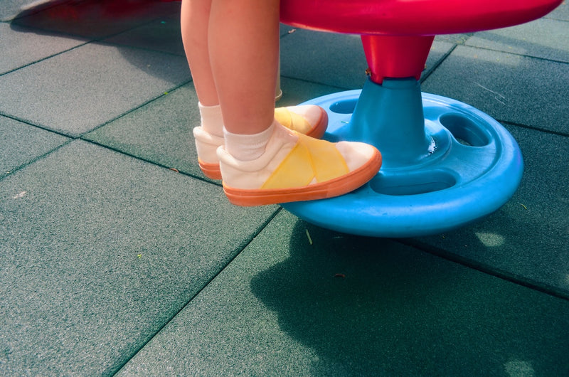 Child's feet in yellow sneakers on a blue and red playground seat.