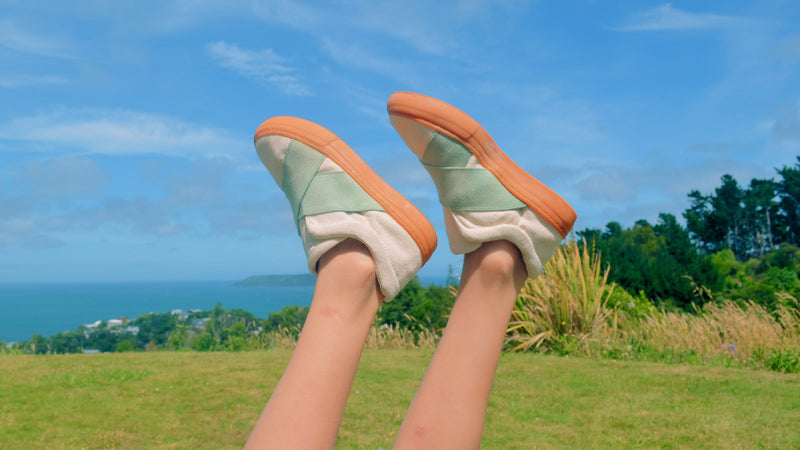 Feet wearing green and brown shoes with a scenic background of ocean and sky.