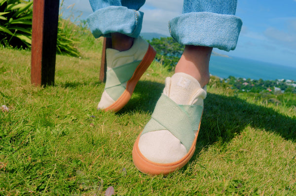 Kid wearing light green shoes with brown soles on grass with a scenic background
